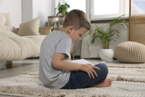 Young Boy Sitting On Carpet Reading As He Slouches