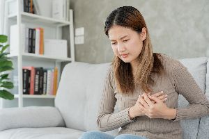 A woman sitting down holding her chest as if she's in pain.