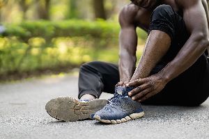 Man sitting on the ground rubbing his sore ankle.